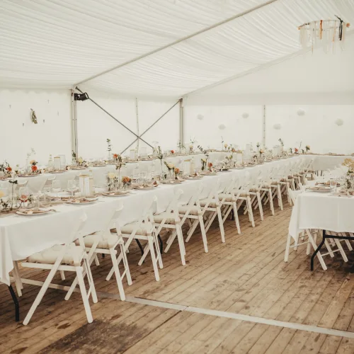 Hochzeit im Zelt - Zelt von innen mit eckigen langen Tischen und Sesseln. Beige & Lachsfarben geschmückt